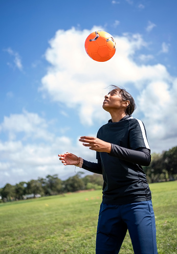 Young female footballer heading the ball while practicing on sports field