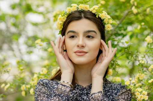 Side view of beautiful girl with flower wreath standing, touching head, looking forward, relaxing. Concept of springtime.