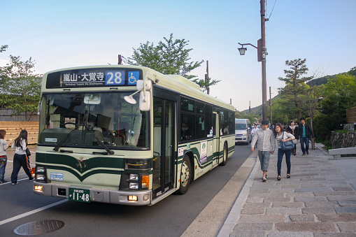 Kyoto, Japan - May 2014: View of Kyoto city bus Number 28 on the road near Tenryu-ji temple with people walking on cobblestone pavement and clear blue sky background.