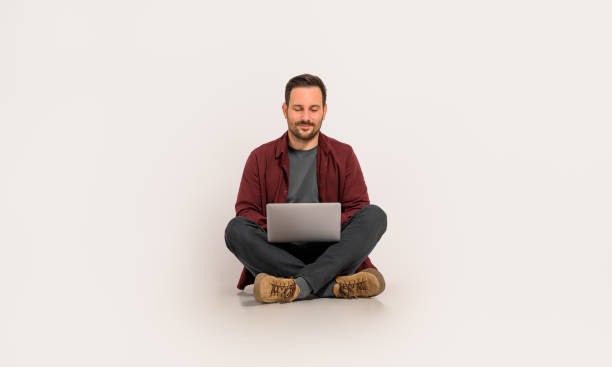 istock Full length of handsome entrepreneur checking e-mails over laptop while sitting on white background 2020033357