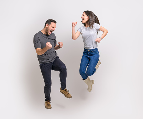 Full length of excited young couple screaming and pumping fists while jumping over white background
