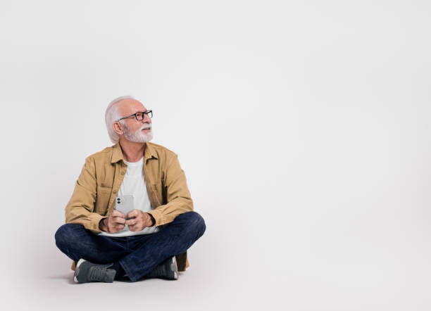 istock Thoughtful senior businessman with mobile phone looking away while sitting over white background 2020033922