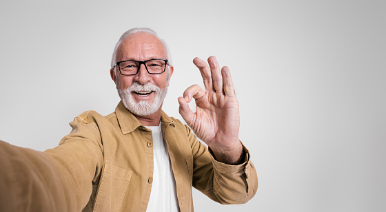 Portrait of senior businessman smiling and showing OK gesture while standing over white background