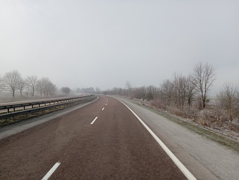 A straight asphalt road with a metal barrier that separates the traffic lanes. Landscape on the highway while traveling by car.