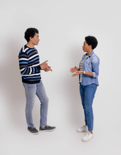 istock Side view of young couple looking at each other and discussing while standing over white background 2020037085