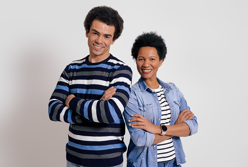 Portrait of confident couple with arms crossed smiling at camera and posing over white background