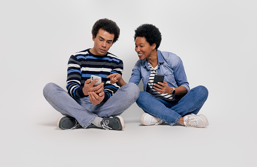 Full length of happy girlfriend pointing at boyfriend's smartphone while sitting on white background