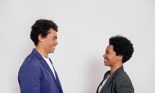Side view of smiling young colleague with afro hairstyle looking at each other over white background