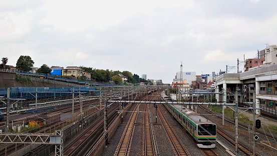 Tokyo, Japan - 10.26.2019: A train passing through a station with empty tracks alongside under a cloudy sky
