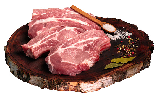 Raw fresh pork meat cut into pieces for frying (pork steak) with spices and salt on a wooden board. Isolated on a white background