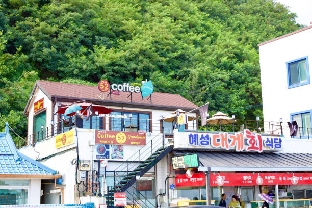 Donghae City, South Korea - July 29th, 2019: Nestled at the base of the hill below the iconic Mukho Lighthouse, coffee shops at Mukho Port offer a serene retreat, with lush green trees on the hillside providing a picturesque backdrop for a leisurely coffee break.