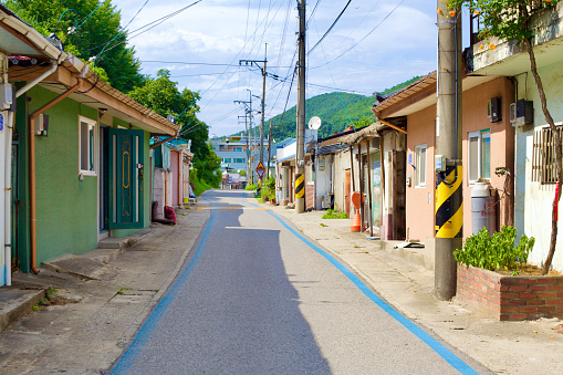 Donghae City, South Korea - July 29th, 2019: A blue-lined bike path meanders through the heart of Mukho Port, flanked by low houses of the fishing community, modest dwellings, electrical poles, and overhead wires, all basked in the warmth of a sunny day.