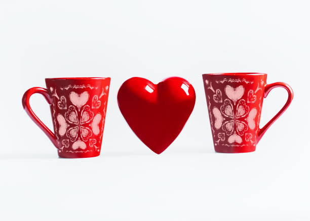 Two red mugs with heart ornament standing on white background. Valentines day or love concept
