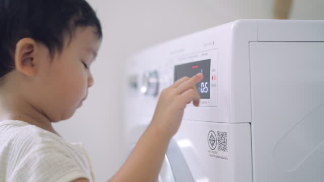 Cute little boy doing laundry at home.Press the start button of the dryer.