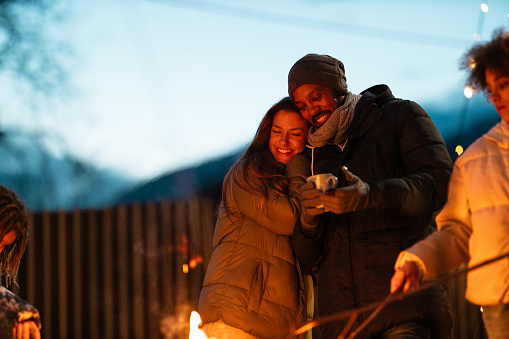 A multiracial couple enjoys Family time around the fire.