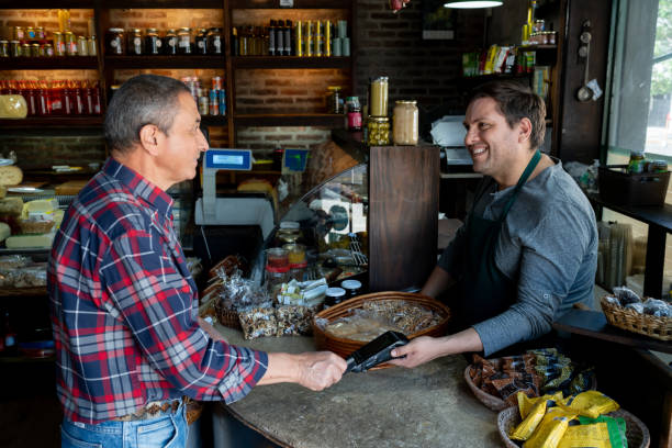 istock Senior customer paying for his products with a credit card while smiling to the friendly salesman at a charcuterie 2020171826