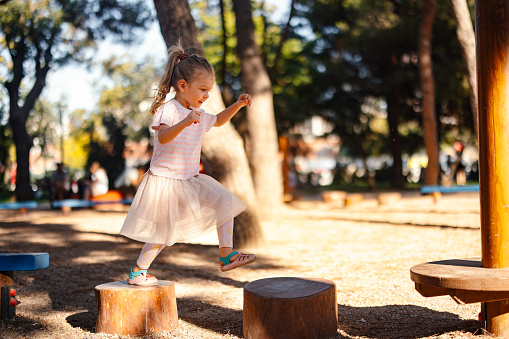 Happy little girl jumping on a tree stump outdoors.