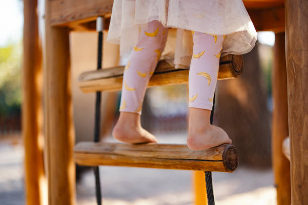 Close up photo of barefoot girl legs climbing on a wooden ladder outdoors.