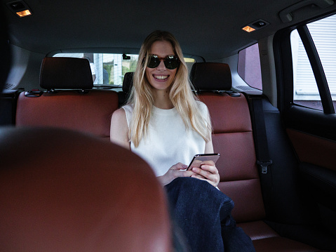 A young blonde girl enjoys talking with a friend on the phone while sitting in a car.