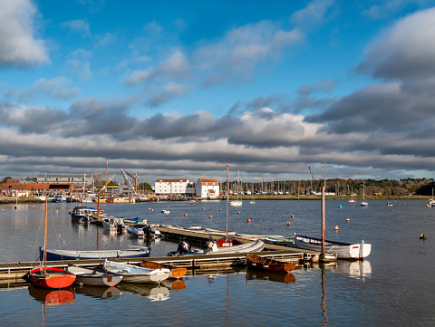 Rowing boats moored at a jetty in Woodbridge, Suffolk, Eastern England. The famous old Tide Mill is in the background where dark clouds threaten rain, despite the bright sunshine.