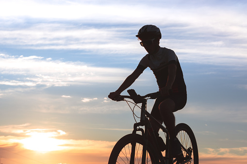 A silhouette of a man riding a mountain bike against a sunset sky. The image portrays the cyclist lifestyle and mountain biking enthusiasts.