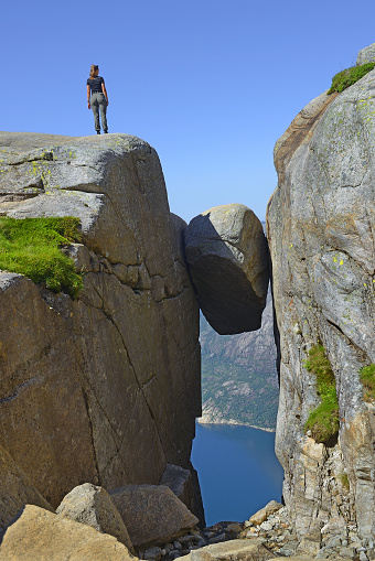 Kjeragbolten, Travel in Norway Kjerag mountains, extreme vacations, adventure where the famous boulder stuck at an altitude of 984 meters above Lysefjorden on Mount Kjerag, Norway - a siulet of one person stands next to a wedged boulder as a measure of its size