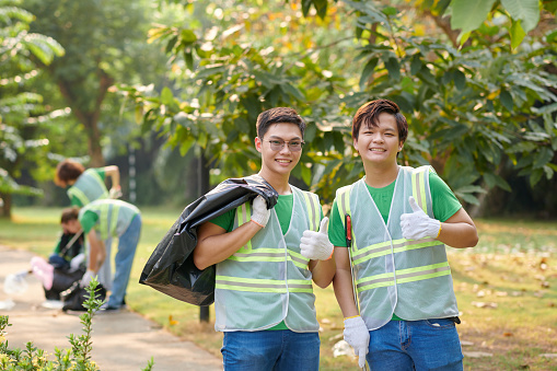 Smiling volunteers with garbage bags showing thumbs up