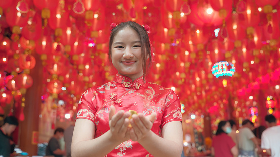 youthful, red-haired Asian girl Cheongsam is give gold ingot at the Chinese temple.for lucky and happy chinese new year.