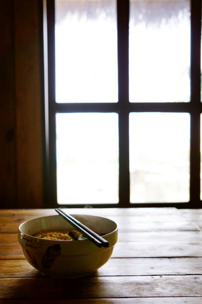 Bowl of hot instant ramen noddles on a table next to a window