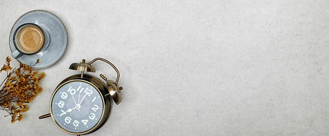 alarm o'clock showing 7 o'clock with cup of milk coffee and gypsophila flowers on gray grunge background