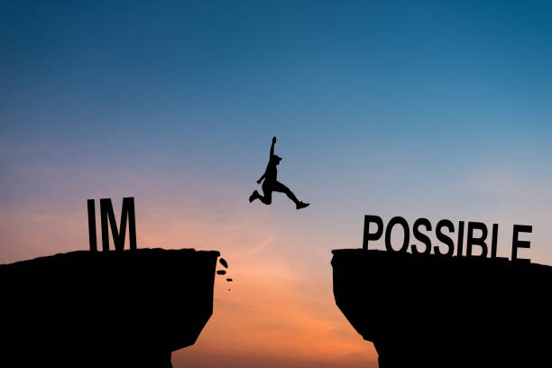 Mindset concept, Silhouette man jumping over impossible and possible wording on cliff with cloud sky and sunlight.