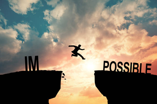 istock Mindset concept, Silhouette man jumping over impossible and possible wording on cliff with cloud sky and sunlight. 2020363461