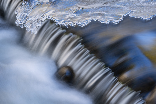 Winter landscape of a cascade captured with motion blur at Bond Falls and framed by ice, Michigan's Upper Peninsula, USA