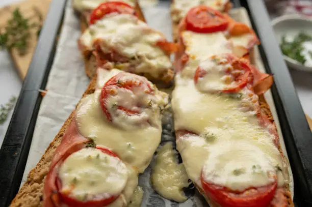 Baked baguette sandwich with italian ham, mozzarella cheese, tomatoes and thyme on rustic bread. Served ready to eat on a baking sheet.