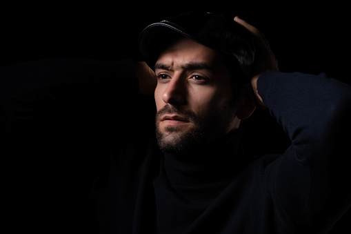 Pensive thinking handsome young beared man portrait Attractive bearded confident guy wear hat looking at blank space Smart man thinking in the dark room Cool man is good looking guy and smart guy