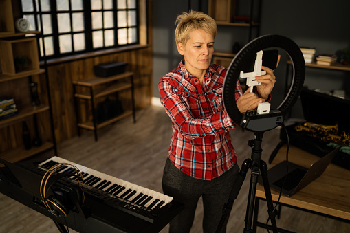 A musician is placing a cellphone into an LED ring light in preparation for a musical vlog for her social media followers