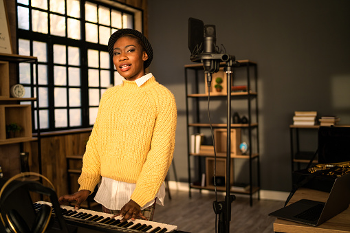 Behind the musical scene, an African-American woman is practising her music on an electric keyboard, in her modern studio
