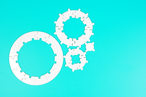Individual components of a circular jigsaw puzzle are arranged like gear cogs against a tranquil blue backdrop. Unity, problem-solving and teamwork related concept.