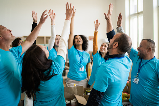 A circle of volunteers happily stretching one arm high in the air at the end of a meeting in a bright light room