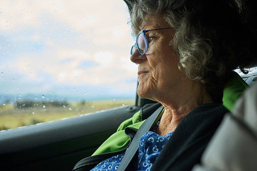Mature woman looking out through the back seat window of a car at the scenic view while driving along a road by the sea