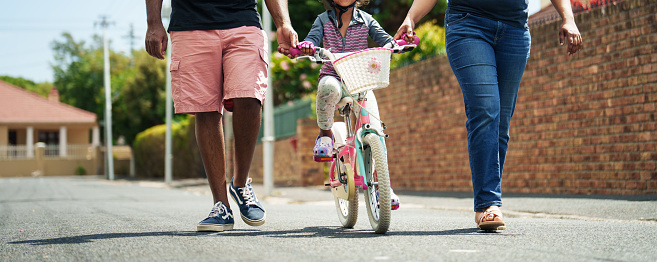 Low angle view of a parents teaching their little daughter how to ride a bike together outside in summer