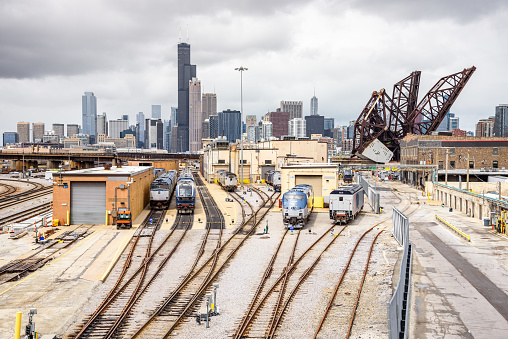 Diesel locomotives at a suburban train depot on a cloudy day. Downtown Chicago skyline and an open draw bridge are in background. Illinois, USA.