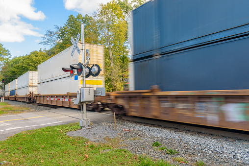 Fast moving container train at a railroad crossing on a sunny autumn morning. Kingston, NY, USA.