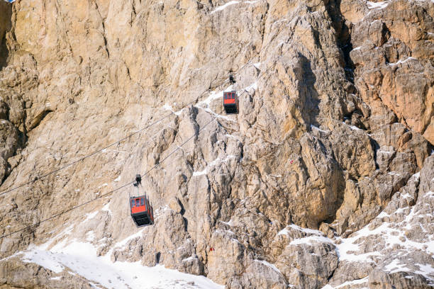 overhead cable car passenger cabins taking people up and down a snowy rocky peak on a sunny winter day - overhead cable car dolomites italy snow imagens e fotografias de stock