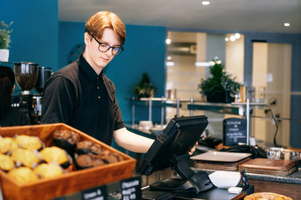 Young waiter serving customer at cash point in cafe. Man working with POS terminal. Student working part-time. Problems of unemployment and Job opportunities for youth. Small business vacancies