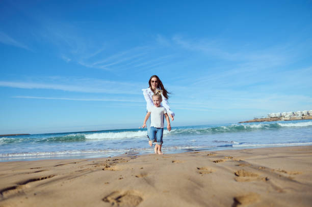 istock Cheerful happy mom catches her daughter while running barefoot, playing together on beach, leaving footsteps on wet sand 2020548815