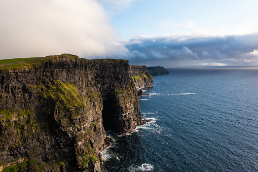 Famous Irish cliffs of Moher in west coast of Ireland with calm and sea water under a cloudy white and blue sky during day.
