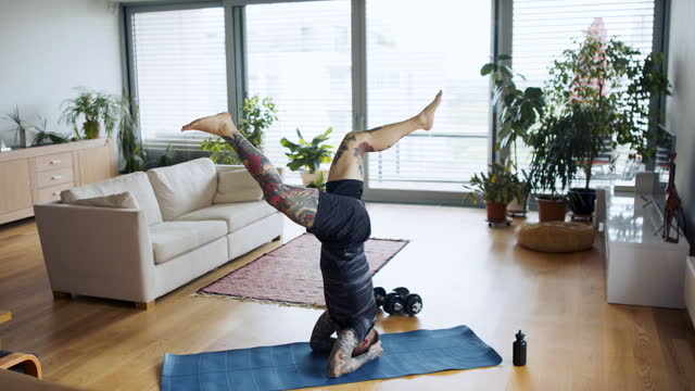Young man doing workout exercise indoors at home, headstand.