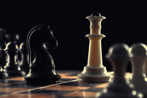 Close-up, chessboard and queen and knight facing each other surrounded by pawns. Retro style