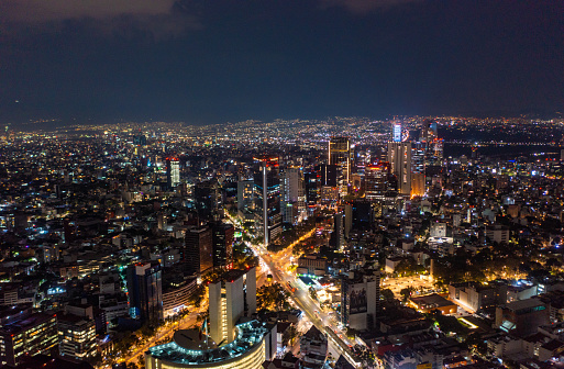 Aerial view of beautiful buildings with illuminated lightings shining in Mexico City against dark black sky at night.